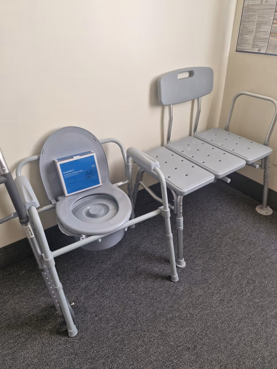 Medical commode chair beside a three-seat hallway bench in a care facility.