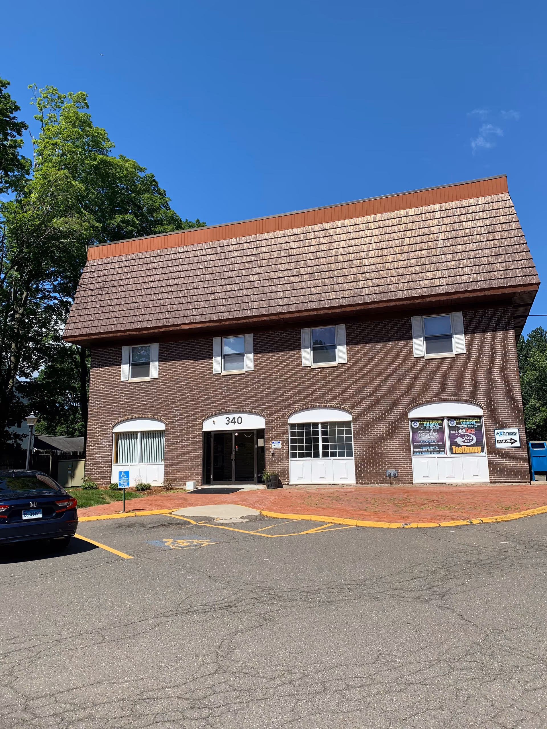 Brick senior living building with arched entrance, multiple windows, and a parking lot in front.
