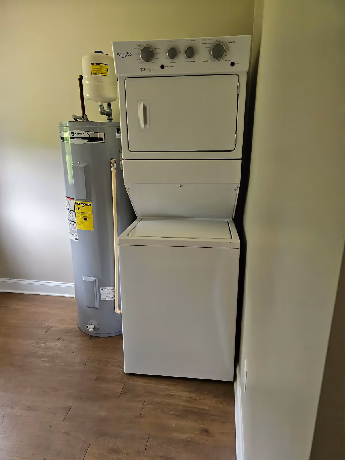 Stacked washer and dryer next to a water heater in a small utility room.