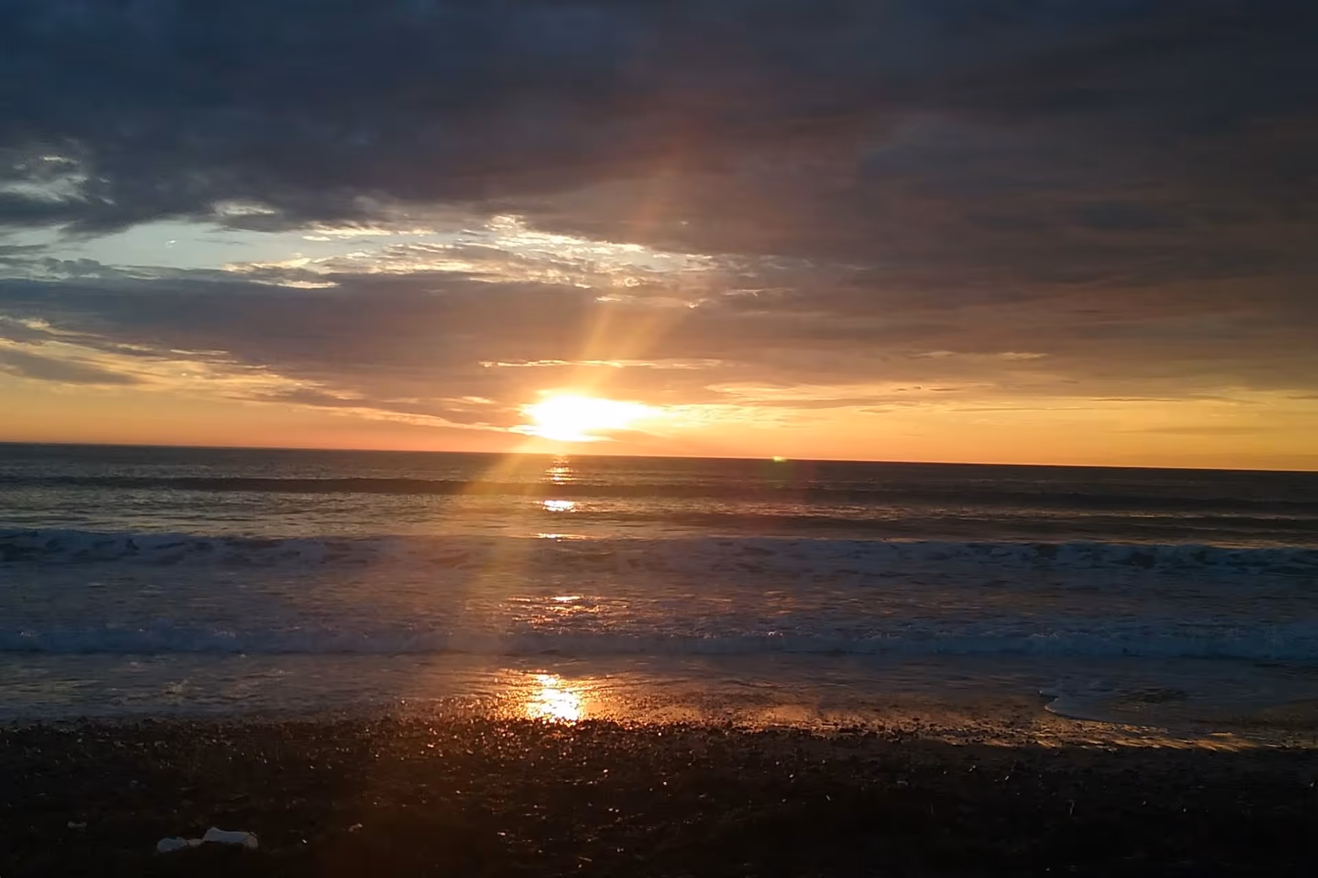 Sunset over the ocean with golden reflection on waves and a dark cloudy sky.