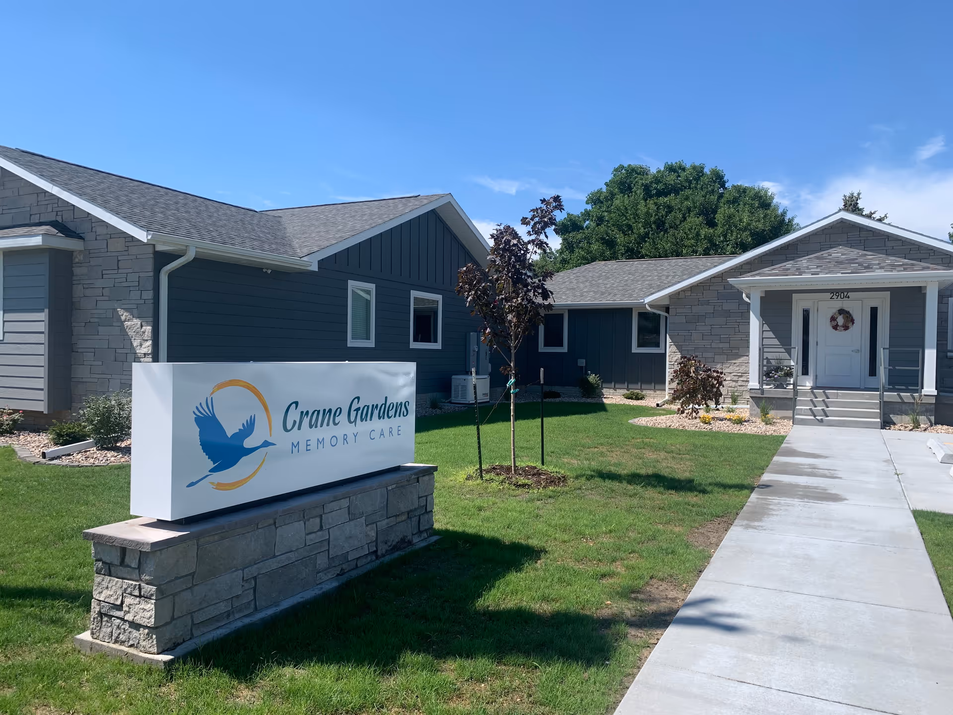 Exterior view of Crane Gardens Memory Care building with sign and walkway
