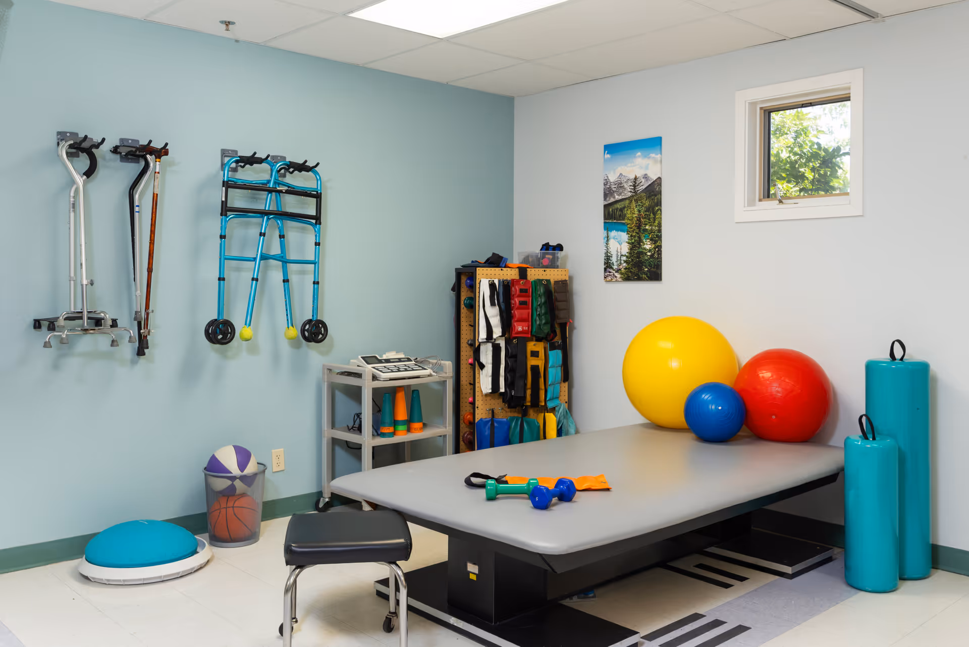 Therapy room featuring a treatment table, exercise gear, and wall-mounted walking aids.