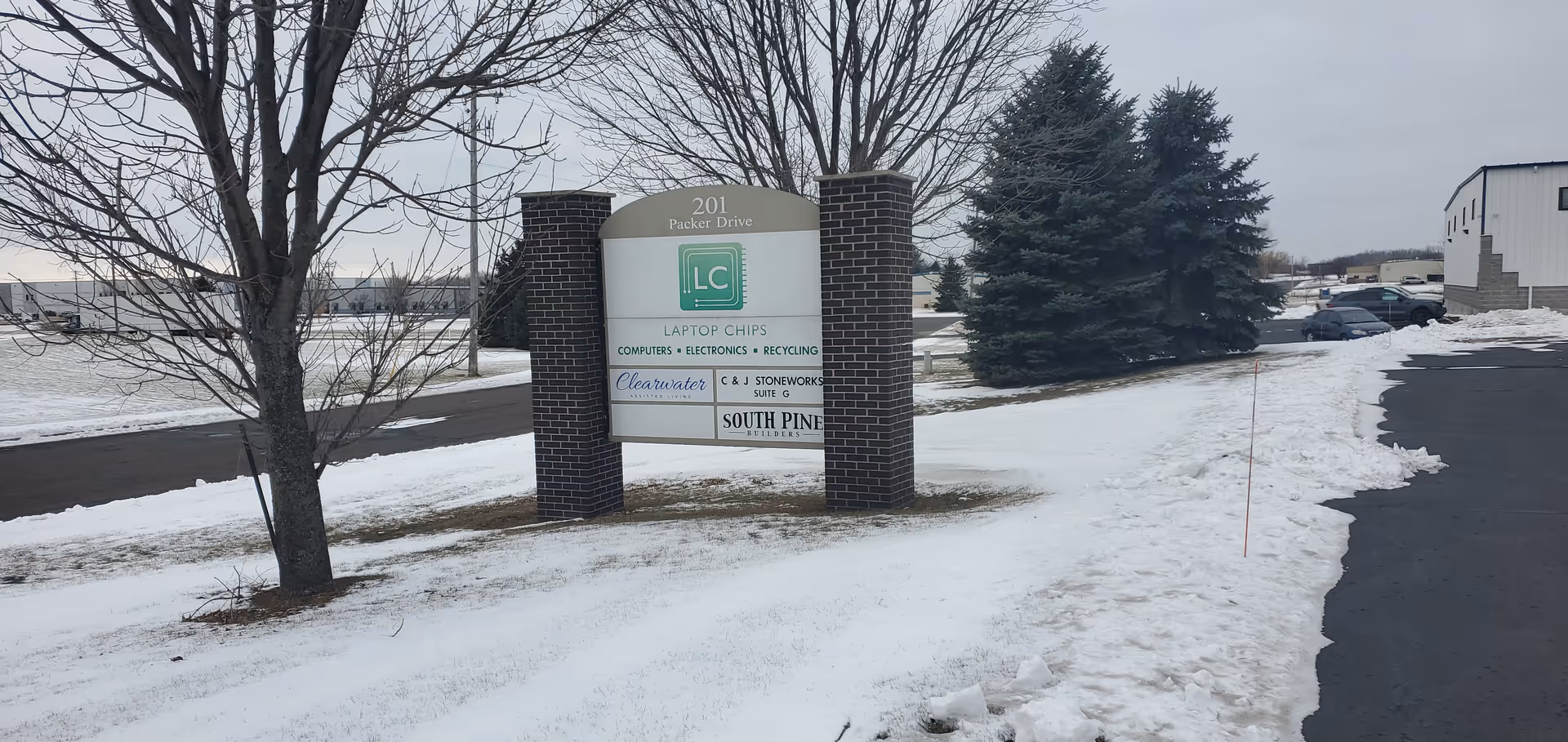 Exterior sign for Clearwater Assisted Living at a snowy roadside with trees and a building nearby.