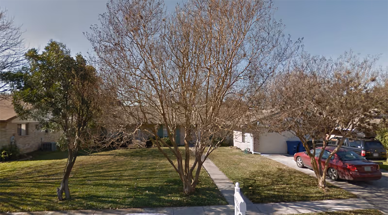 Exterior view of a senior living facility with lawn, trees, and parked cars