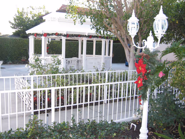 White gazebo and fenced patio area in a garden with a decorated lamp post and surrounding greenery.