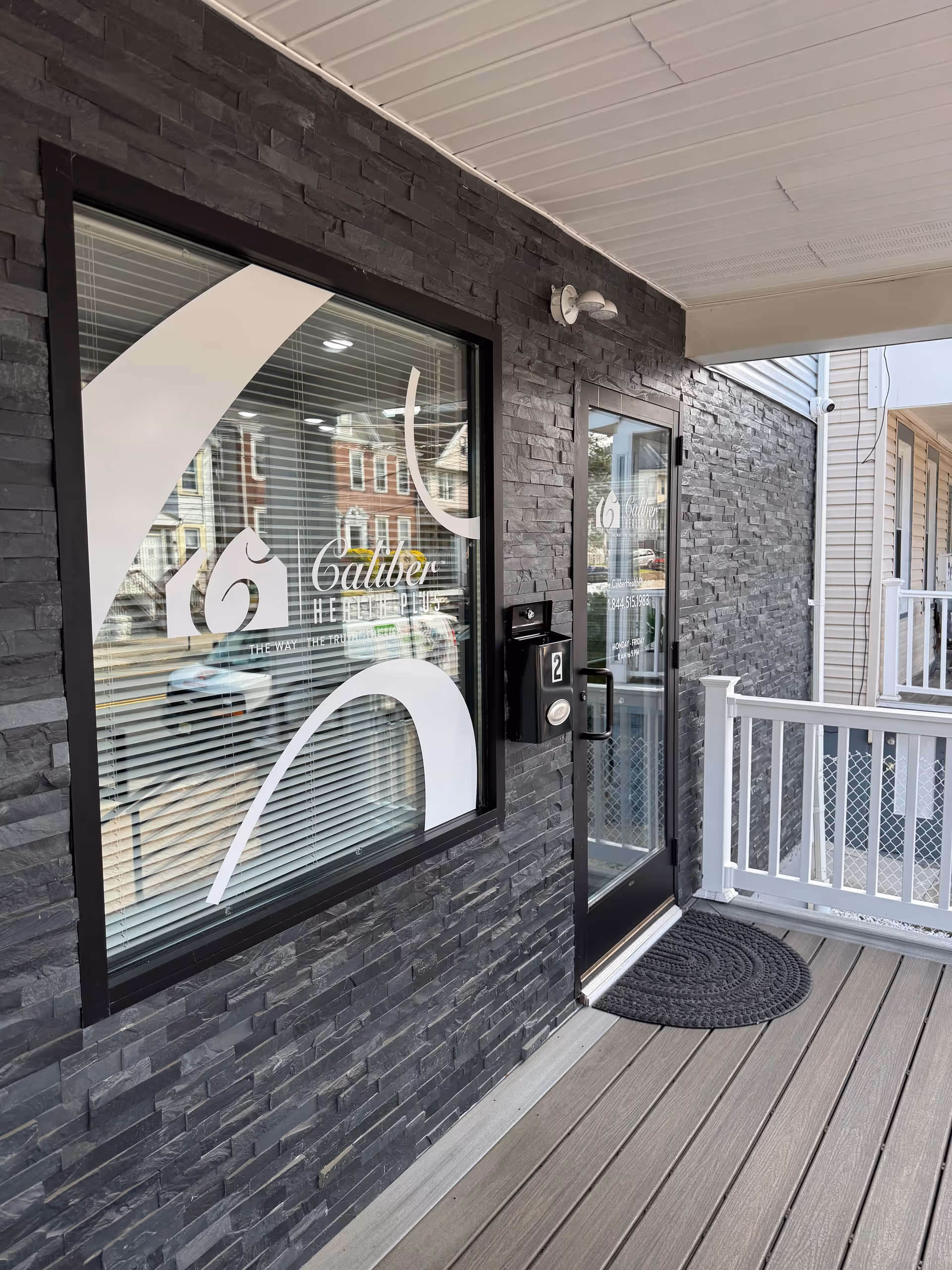 Stone-clad exterior with glass entrance, branding on window, and front porch mat.