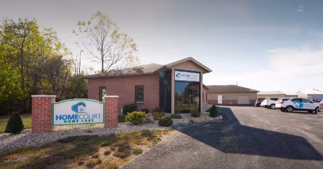 Front view of a brick senior care facility with a HomeCourt sign and parking lot.