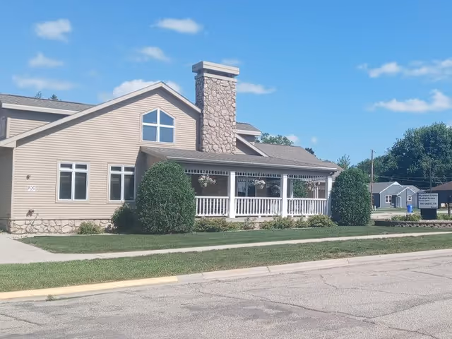 Exterior view of a beige senior living facility with a covered porch and landscaped yard.