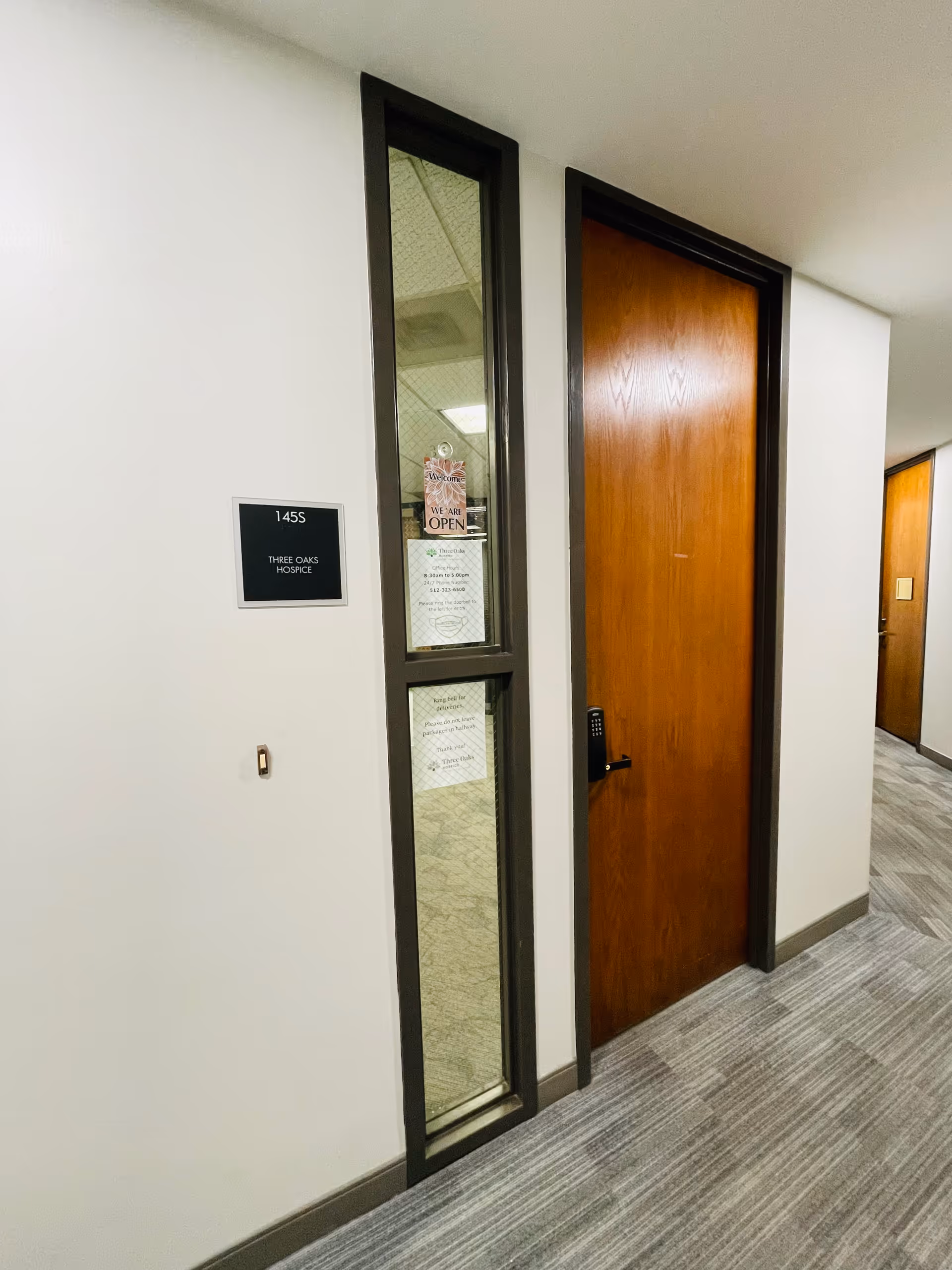 Interior hallway with a wooden door and glass panel entrance to Three Oaks Hospice.