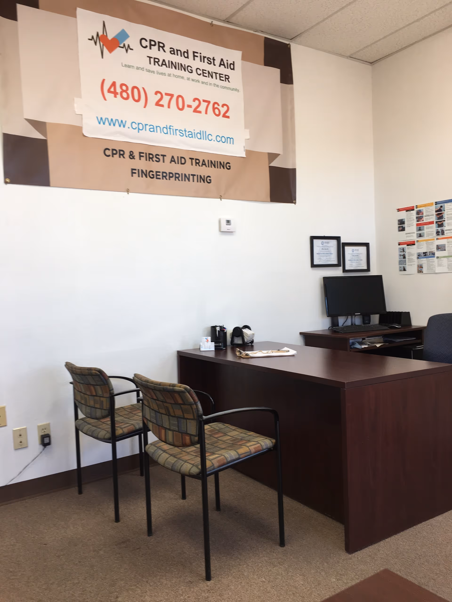 Office area with banner, desk, computer, and two patterned chairs.