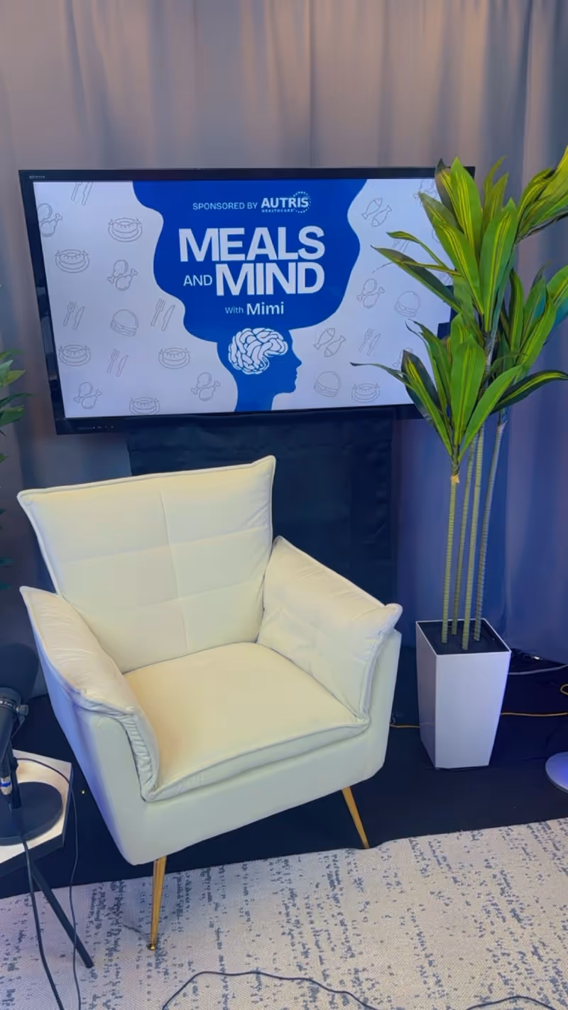 White armchair beside a large screen displaying Meals and Mind with a tall plant nearby.