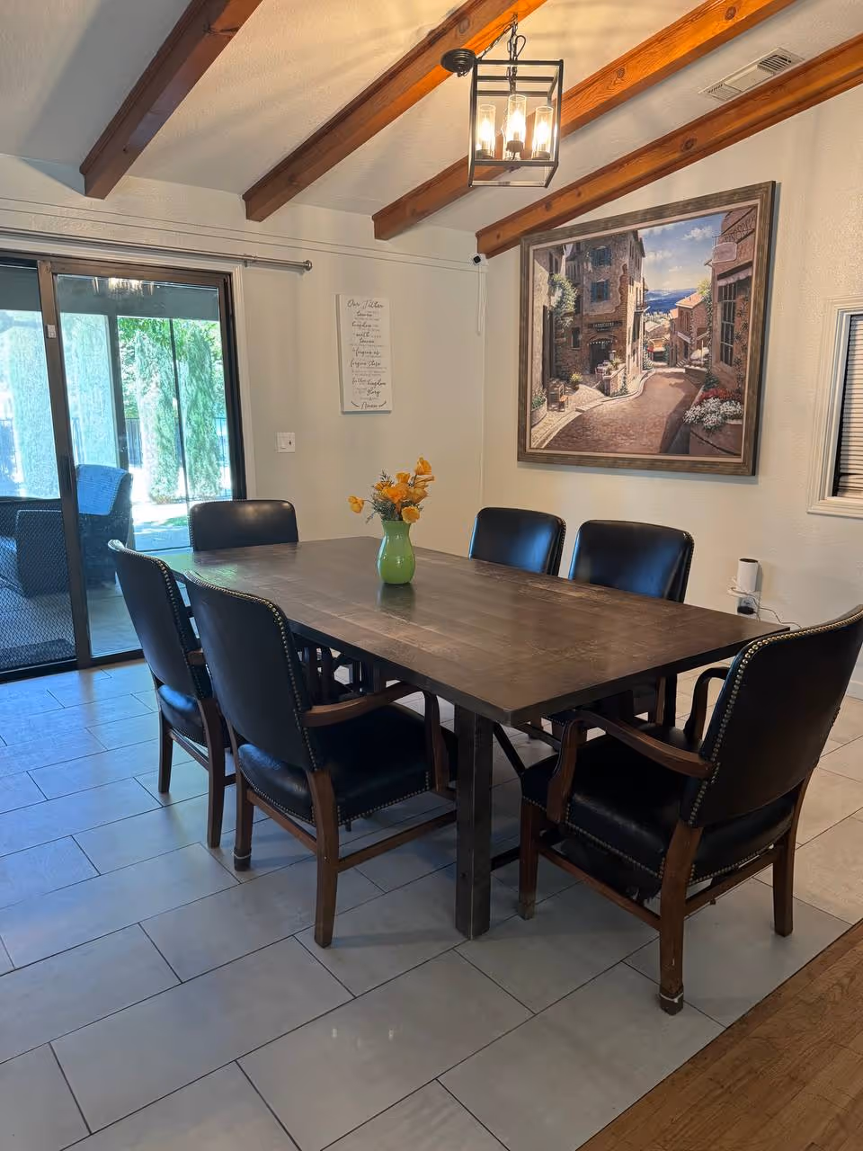 A wooden dining table with eight black leather chairs in a well-lit dining room.
