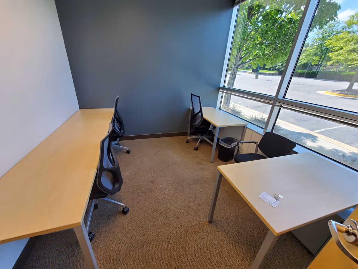 Office-like study area with multiple desks and chairs by large windows overlooking trees