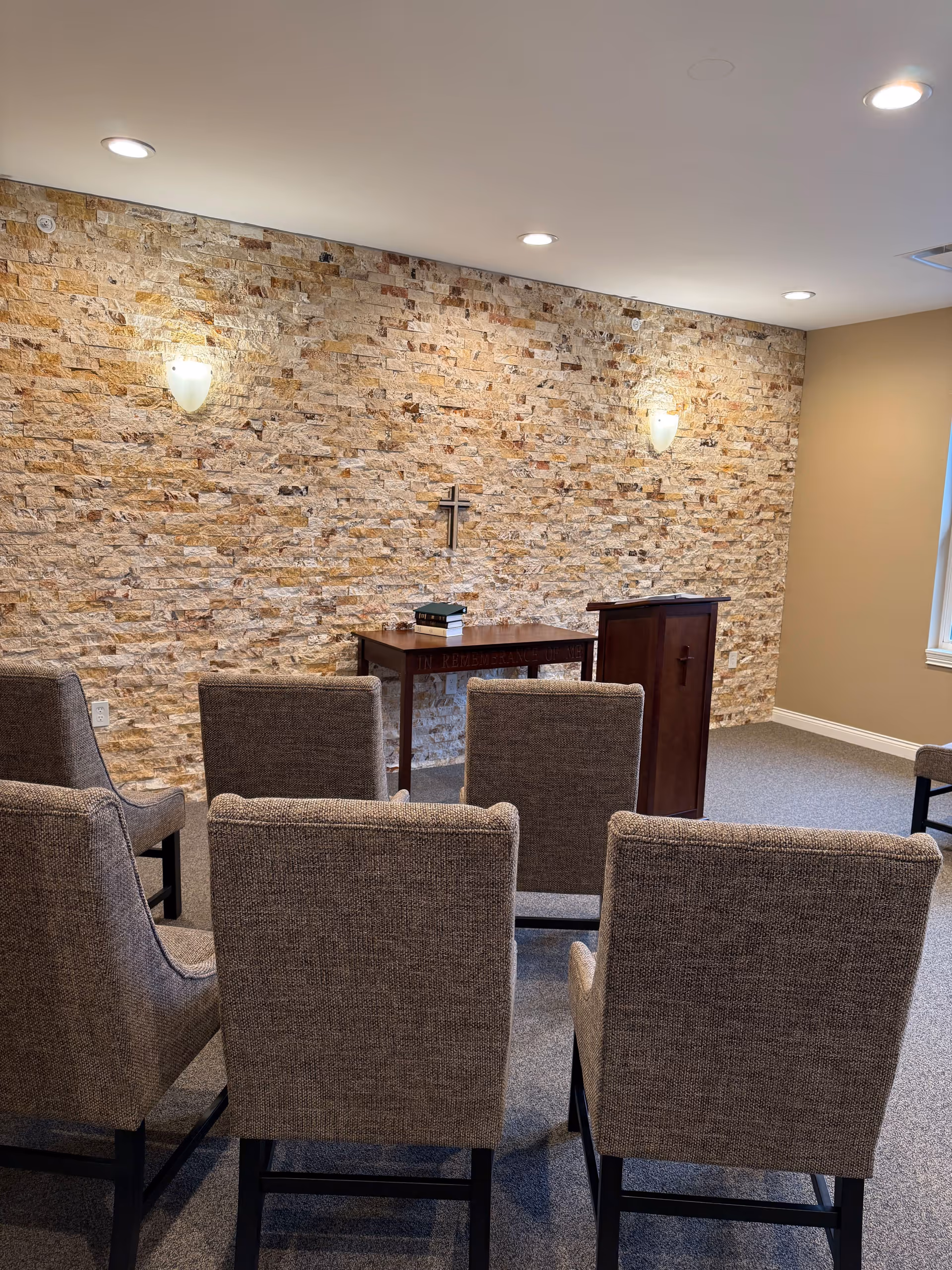 Chapel area in a senior living facility with a stone wall, cross, podium, and chairs.
