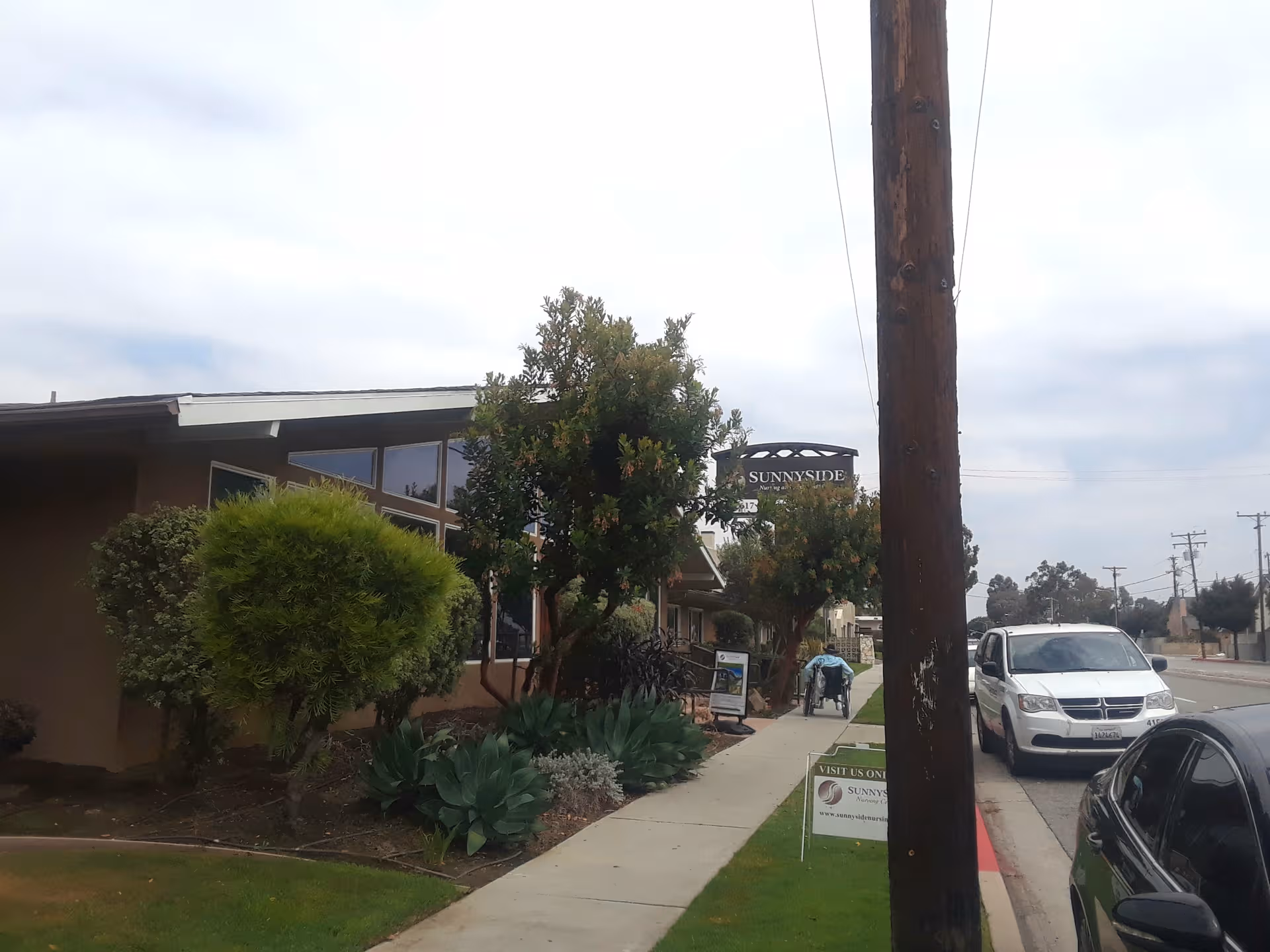 Exterior view of Sunnyside Nursing and Post Acute Care Center with sidewalk, plants, and street.
