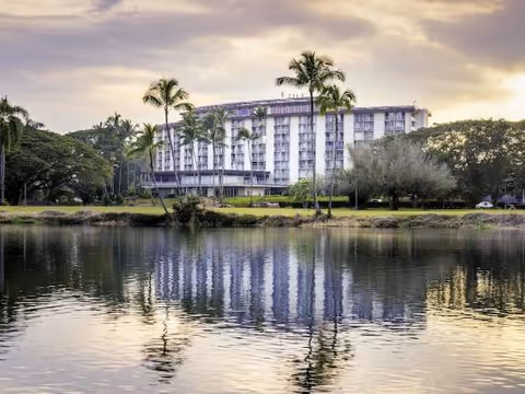 Exterior view of a multi-story senior living facility by a lake with palm trees.