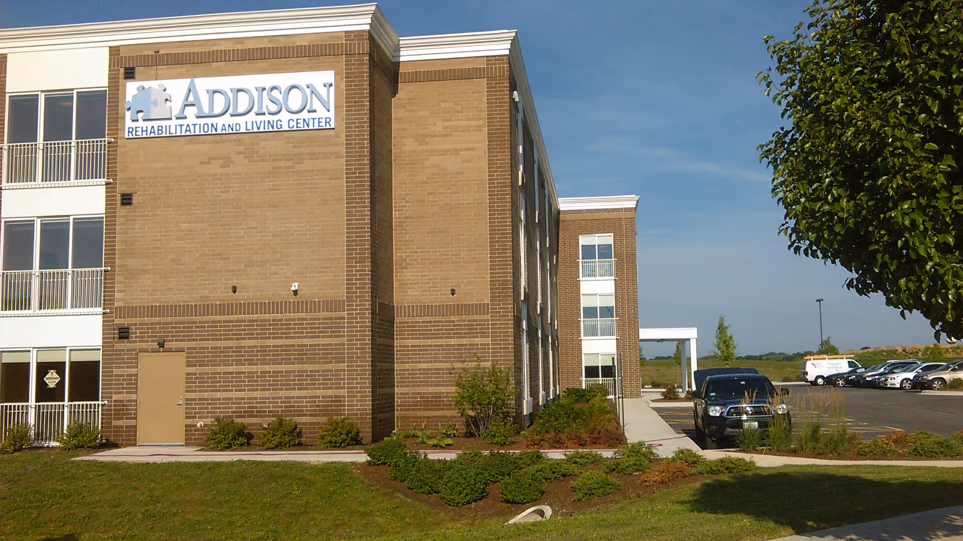 Exterior view of a brick senior living facility with a sign and parked cars.