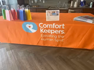 Orange Comfort Keepers table with gift bags and brochures inside a facility.