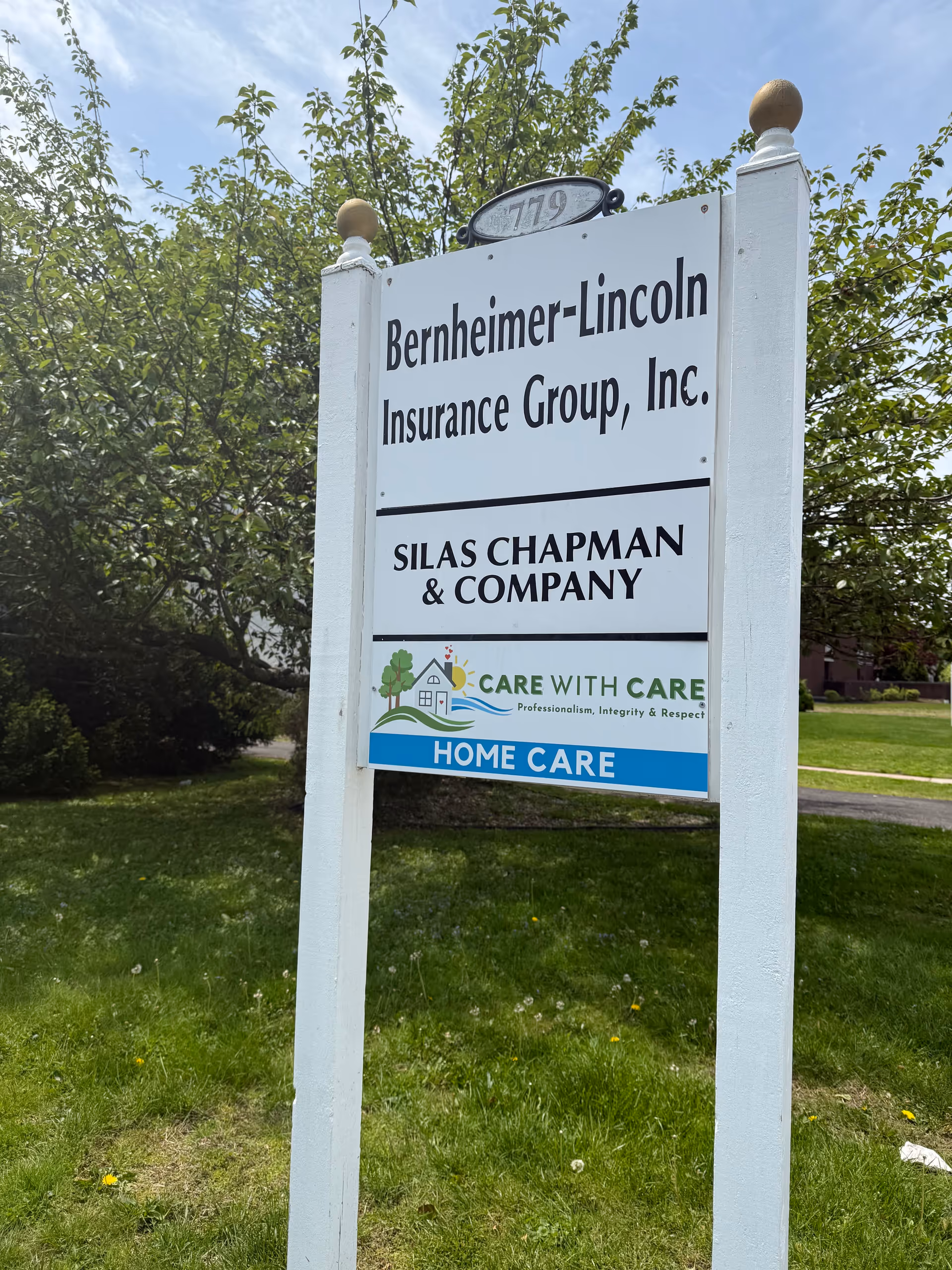 Outdoor signpost displaying Care With Care Home Care and insurance group signage on grassy lawn