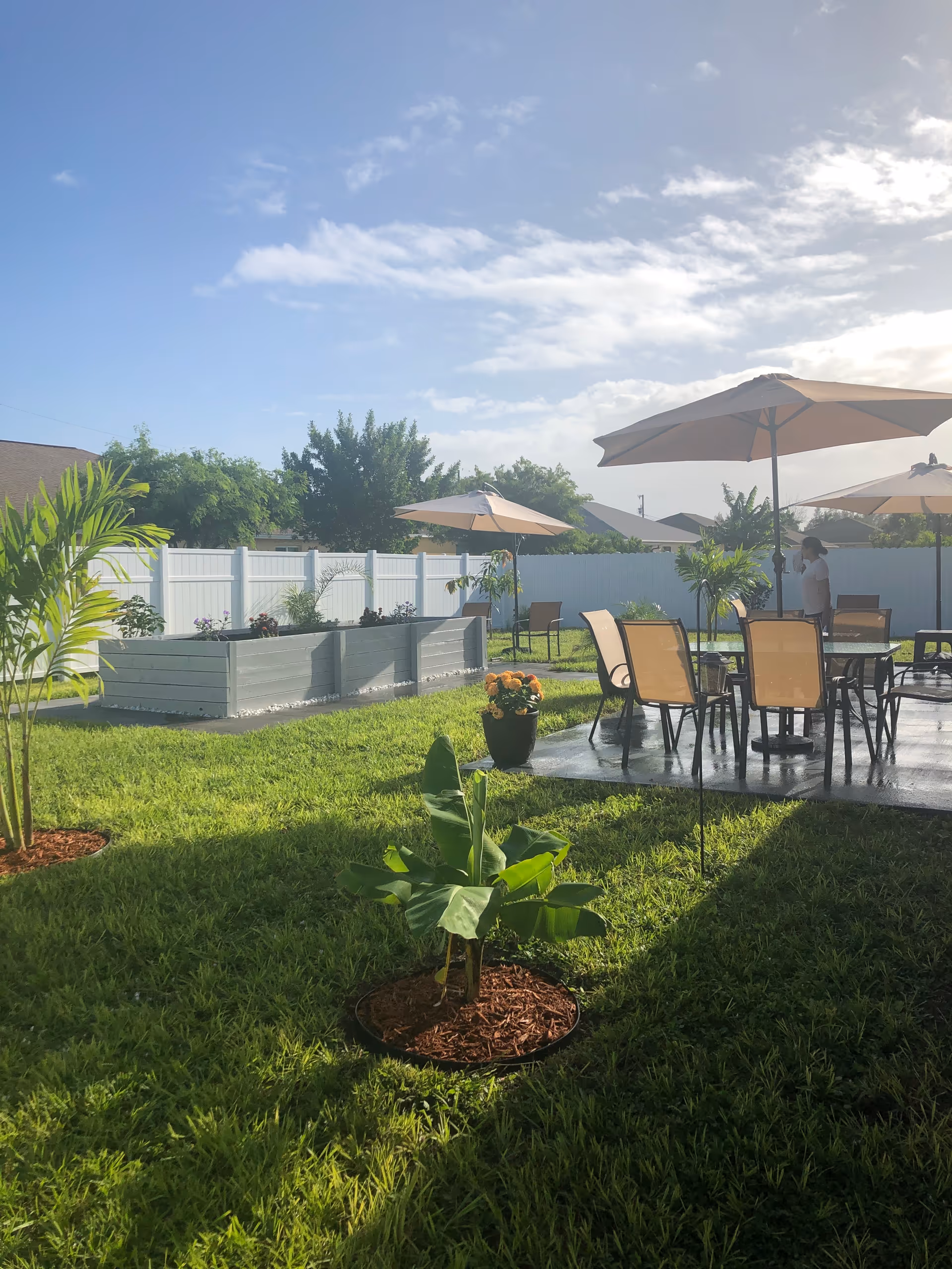 Outdoor patio with chairs, tables, umbrellas, and lush lawn at Love Assisted Living Facility Cape Coral.