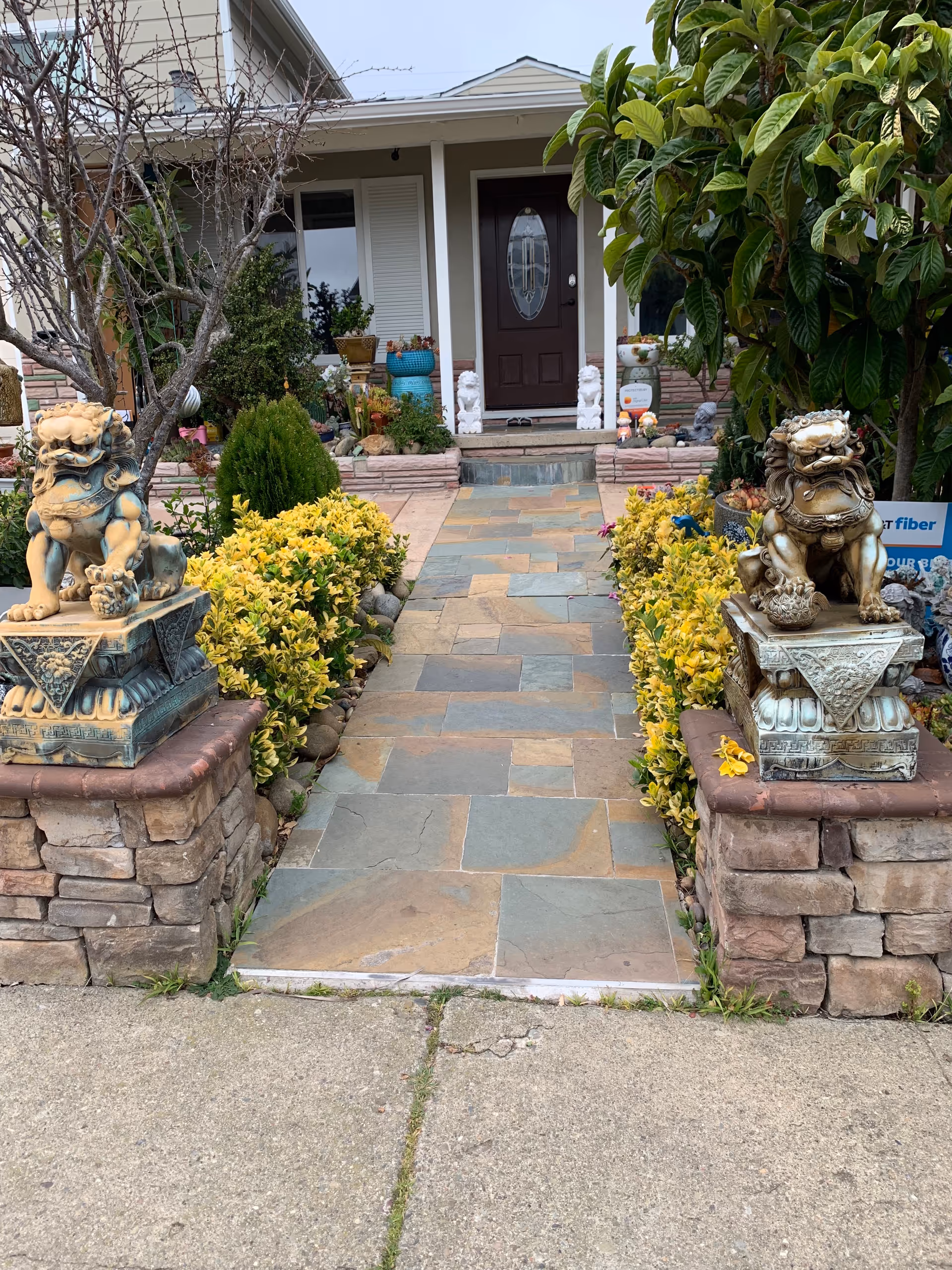 Stone-paved walkway leads to a front entrance framed by statues and lush plants.