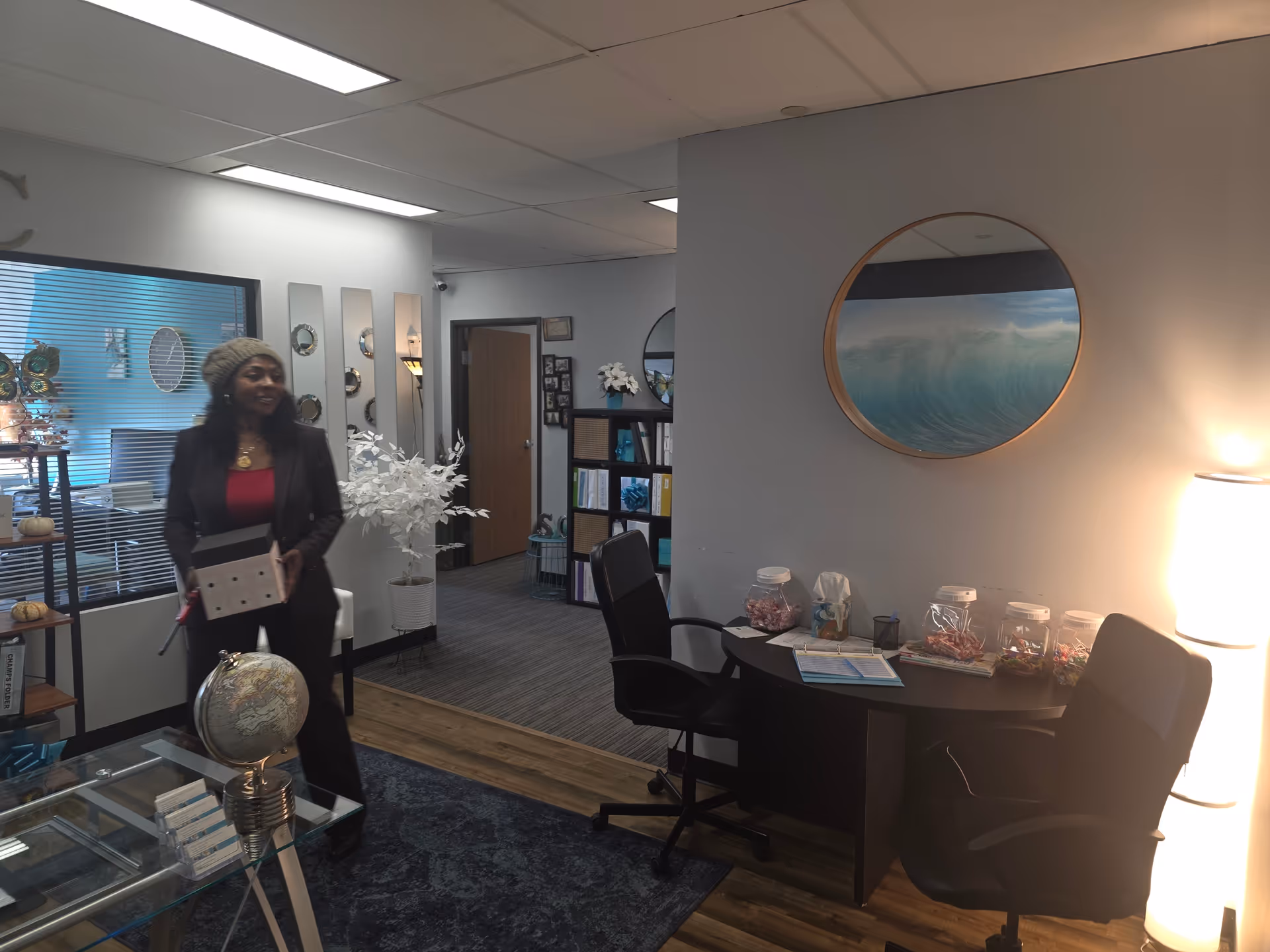 A staff member stands in an office area with a round ocean picture on the wall.