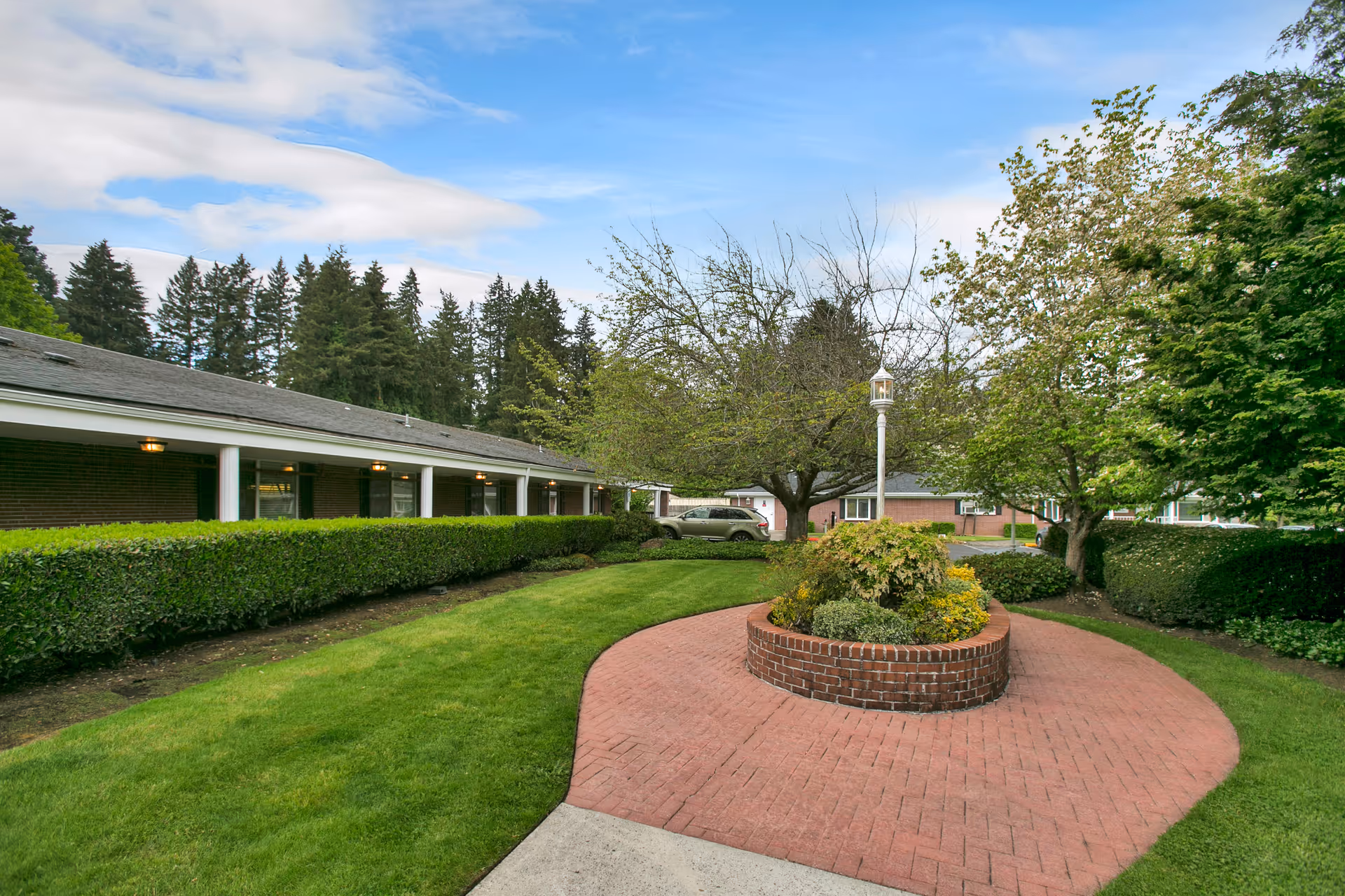 Brick circular walkway surrounds a raised garden in a manicured facility courtyard.