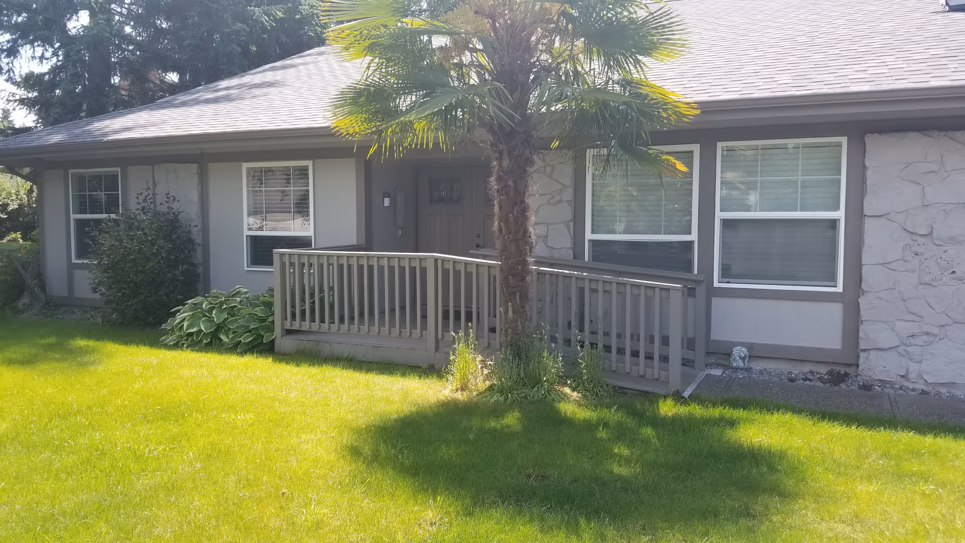 Front view of a single-story senior living facility with a small porch and palm tree.