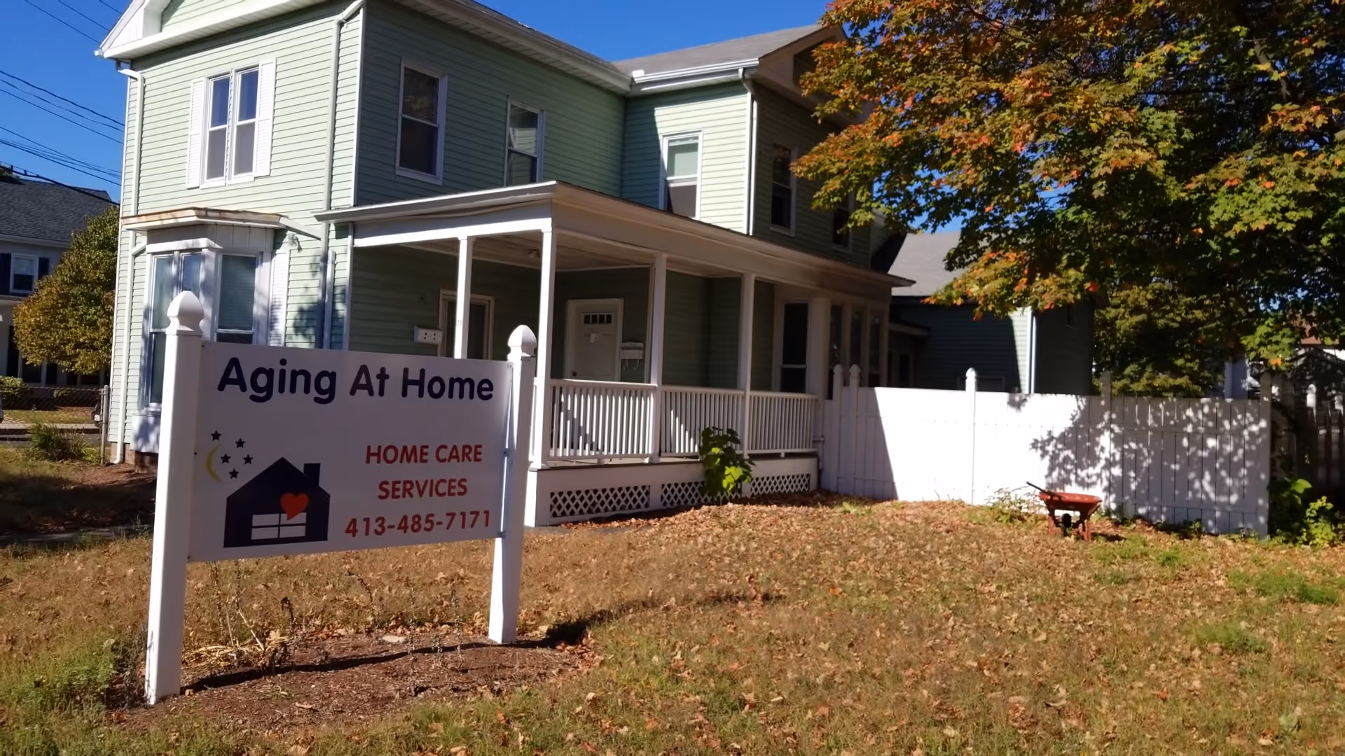A two-story green house with a white porch and a sign reading Aging At Home.