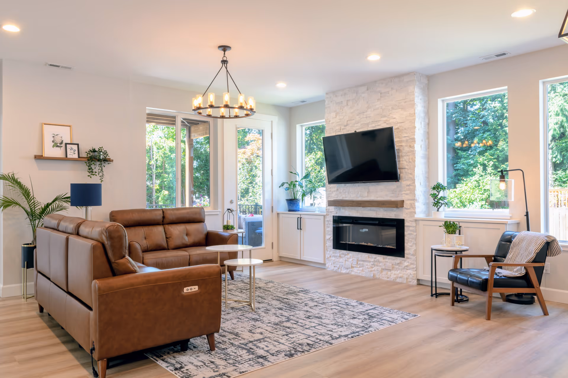 A modern senior living lounge with leather sofas, a fireplace, wall-mounted TV, and large windows.