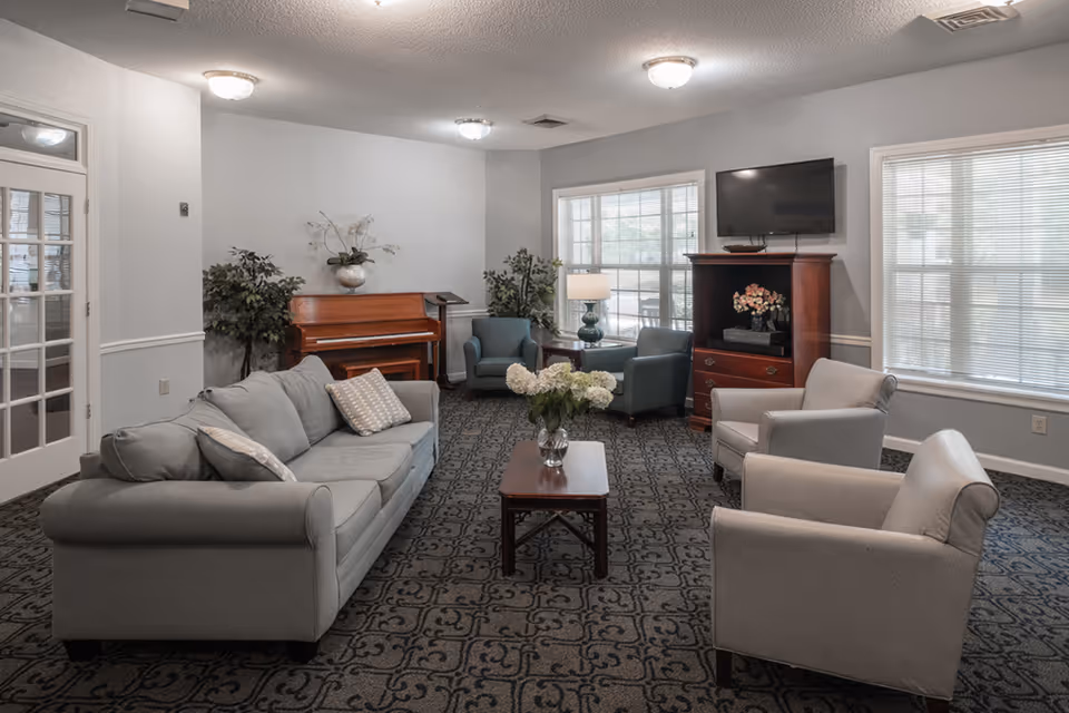 A comfortable common living room with sofas, chairs, piano, fireplace, TV, and windows.