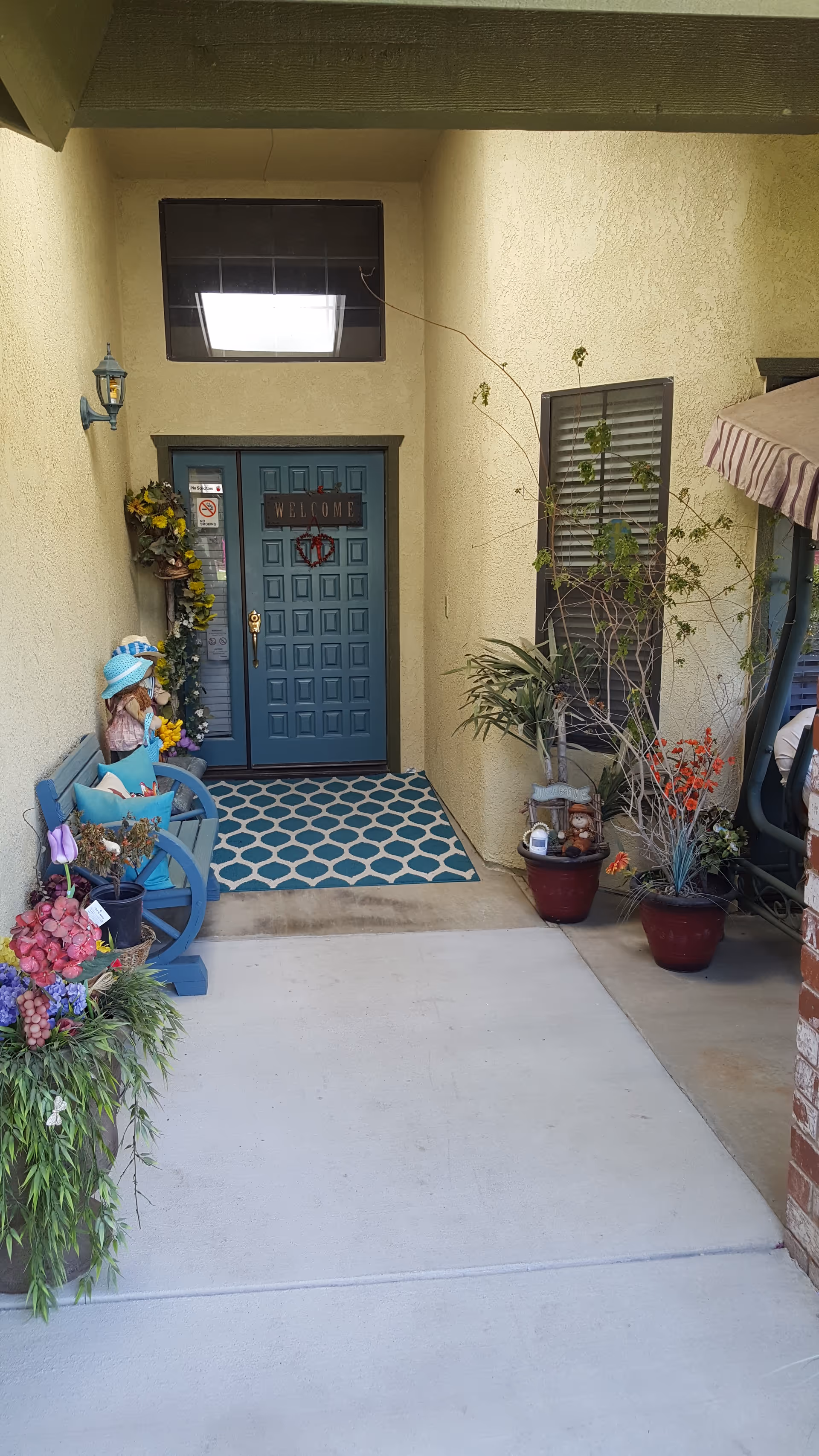 Front entrance of a beige building with a blue door, plants, and welcoming decorations.