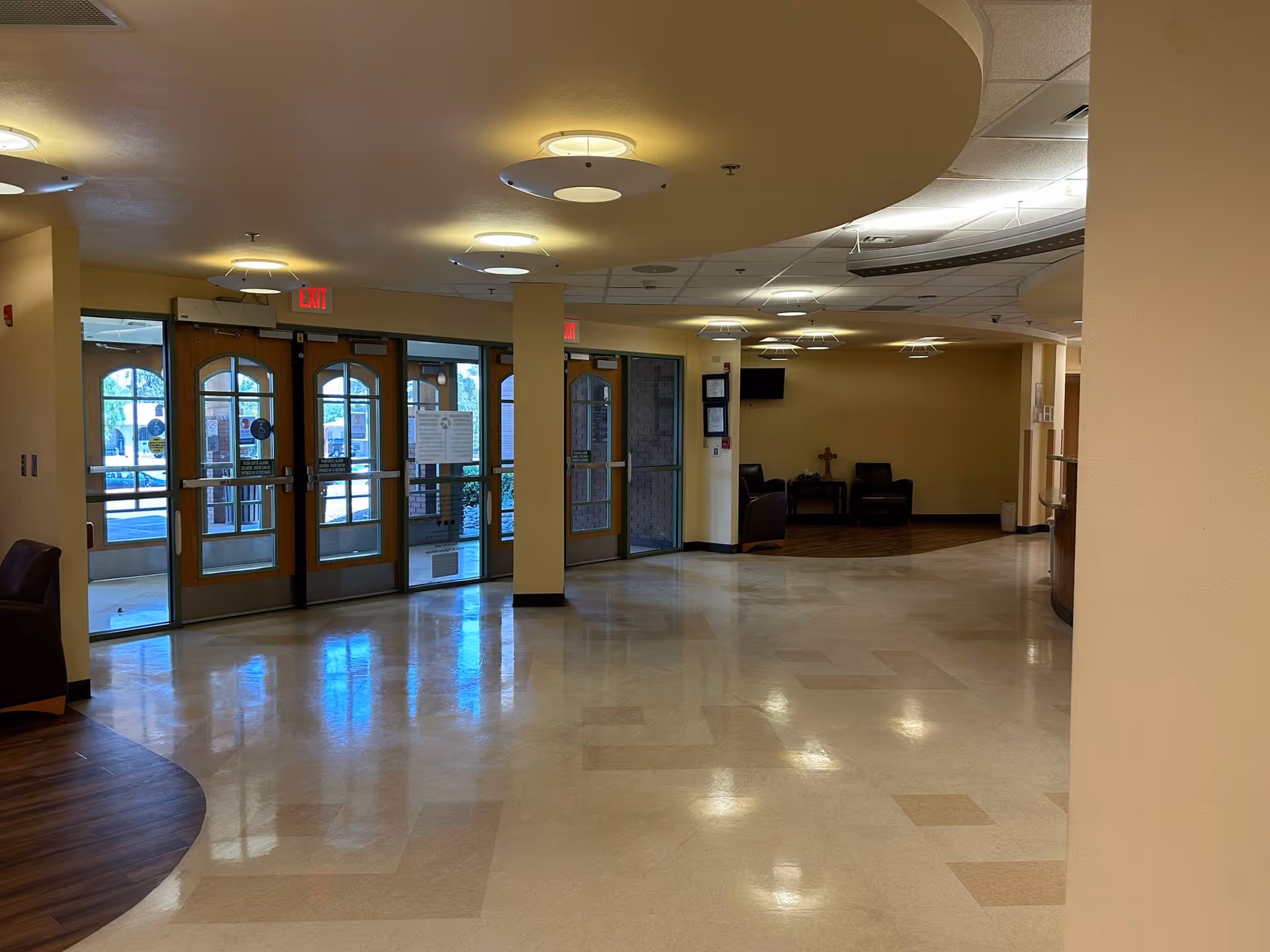 Spacious care center lobby with large glass entrance doors, seating area, and circular ceiling lights reflected on a polished floor.