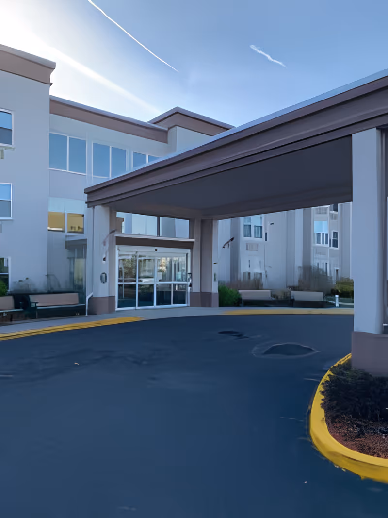 Covered entrance canopy and circular driveway leading to the glass front doors of a multi-story senior living building.