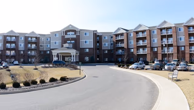 Exterior view of a multi-story senior living building with a curved driveway and parked cars.
