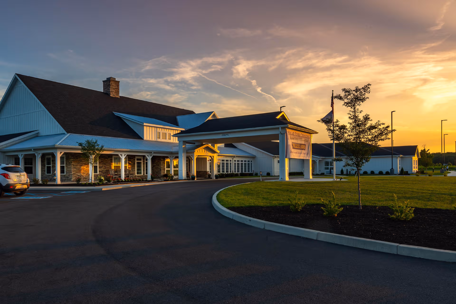 Sunset-lit Sugar Fork Crossing senior living facility with a curved driveway and porte-cochere.