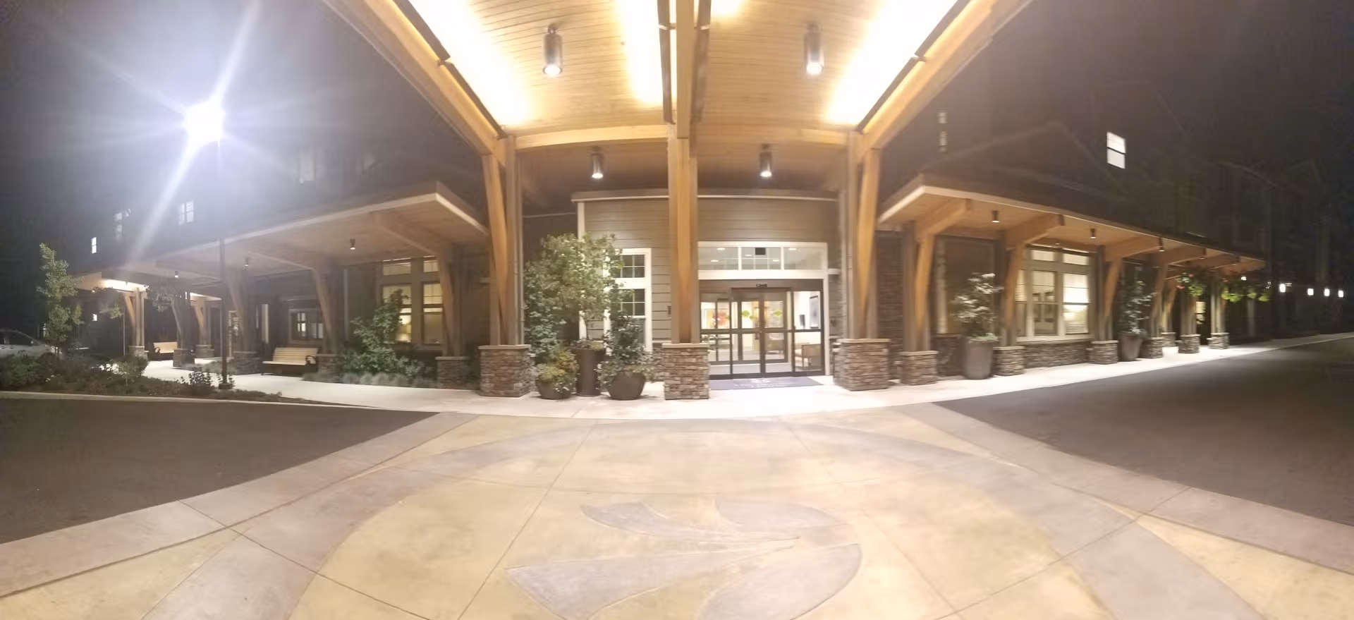 Nighttime exterior view of The Springs at Greer Gardens entrance with wooden columns and planters.