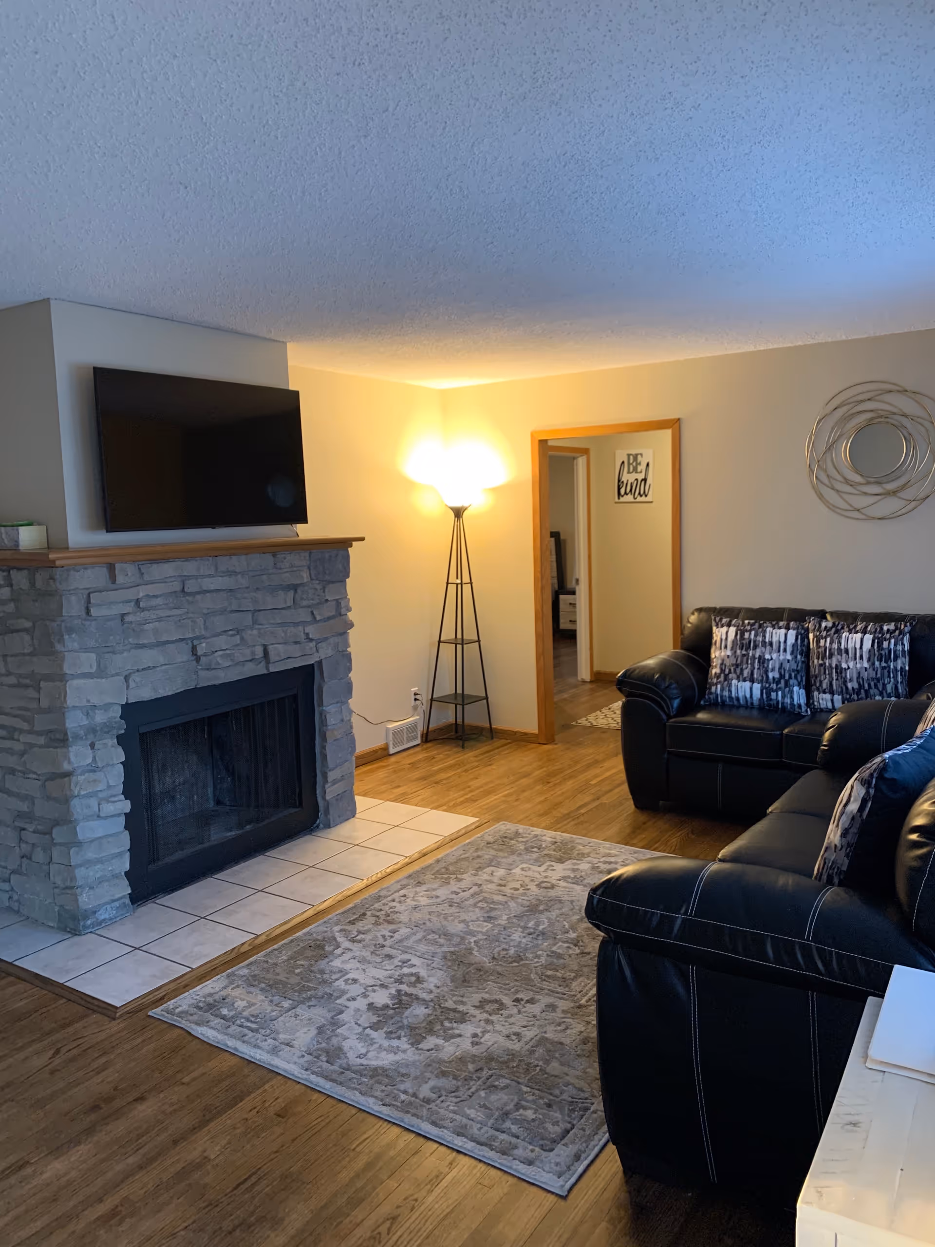 Cozy living room with stone fireplace, mounted TV, leather sofa, rug, and doorway.