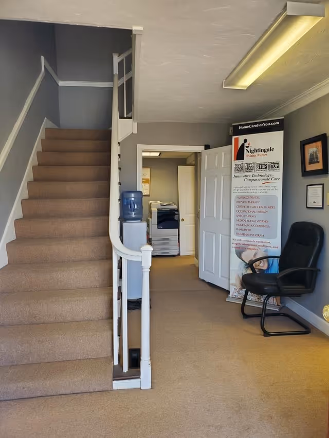 Interior hallway with staircase, water cooler, doorway, and Nightingale Visiting Nurses banner.
