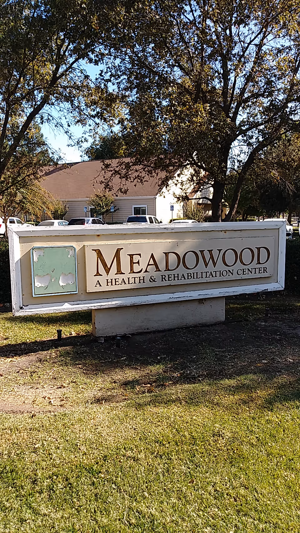 A Meadowood A Health and Rehabilitation Center sign outdoors with a building and trees behind.