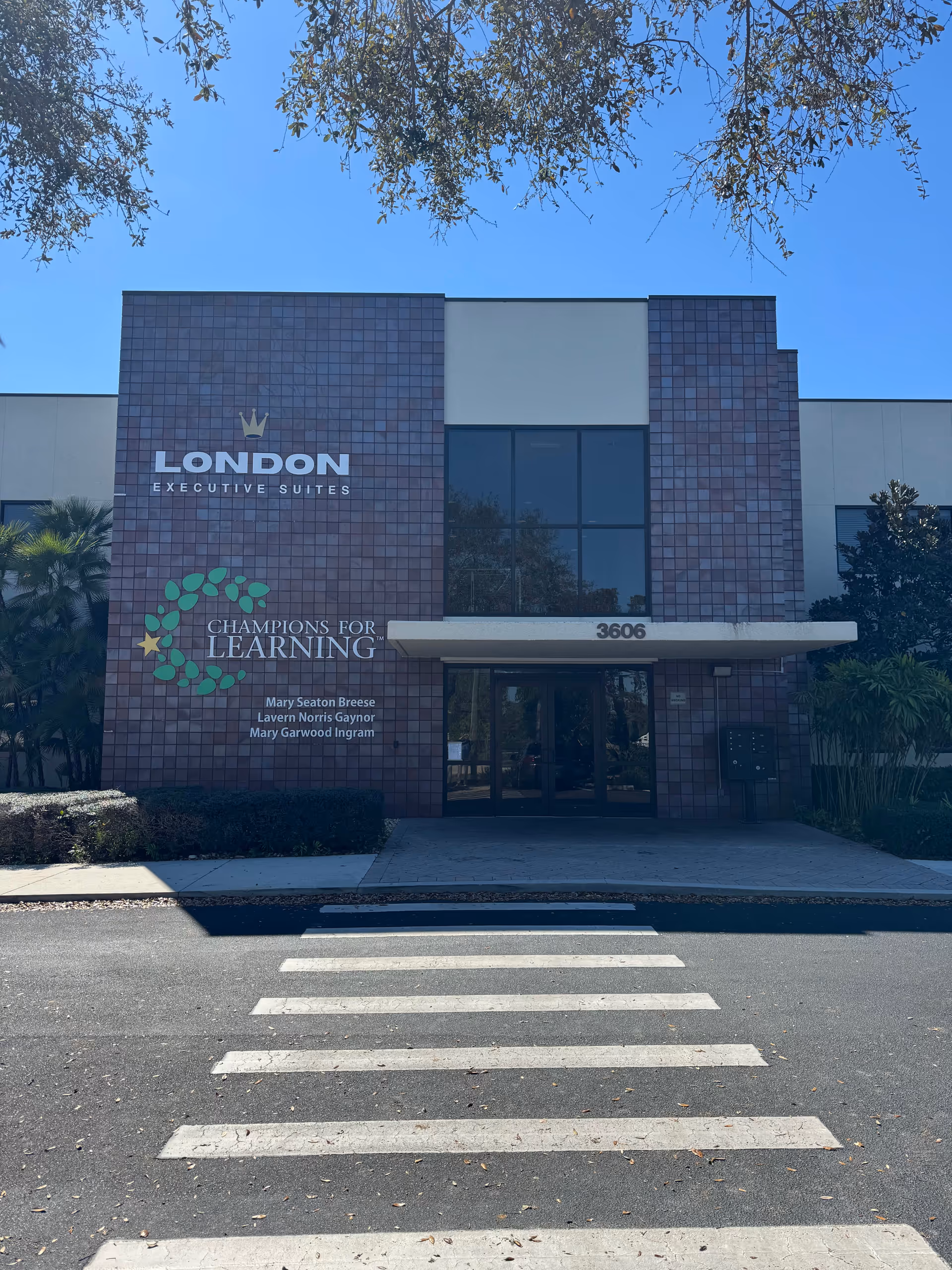 Front of a modern brick building with large glass doors and a crosswalk.