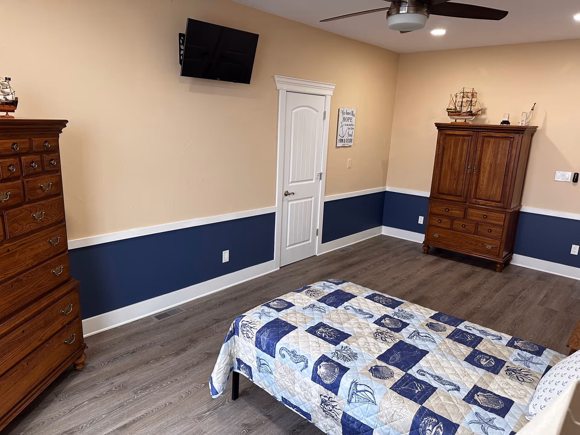 A memory care bedroom with two wooden dressers, a bed, and blue walls.
