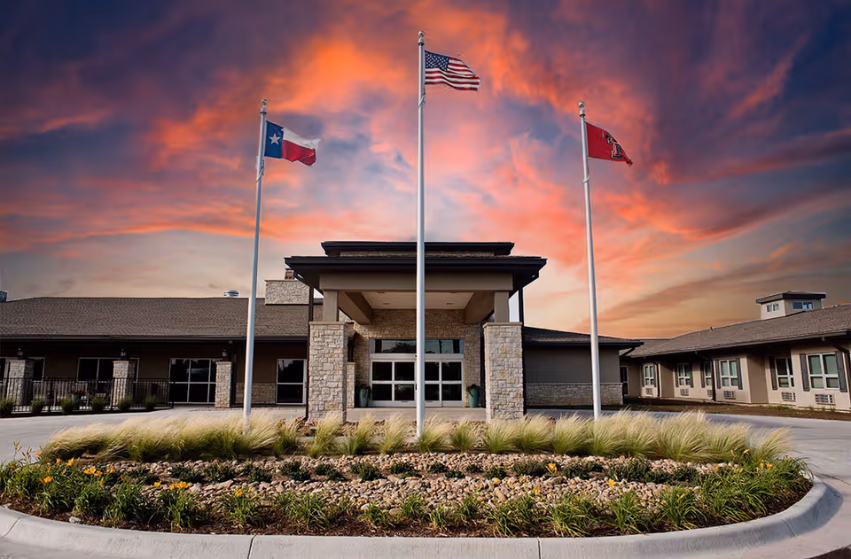 Exterior view of a senior living facility with flagpoles and landscaped entrance.