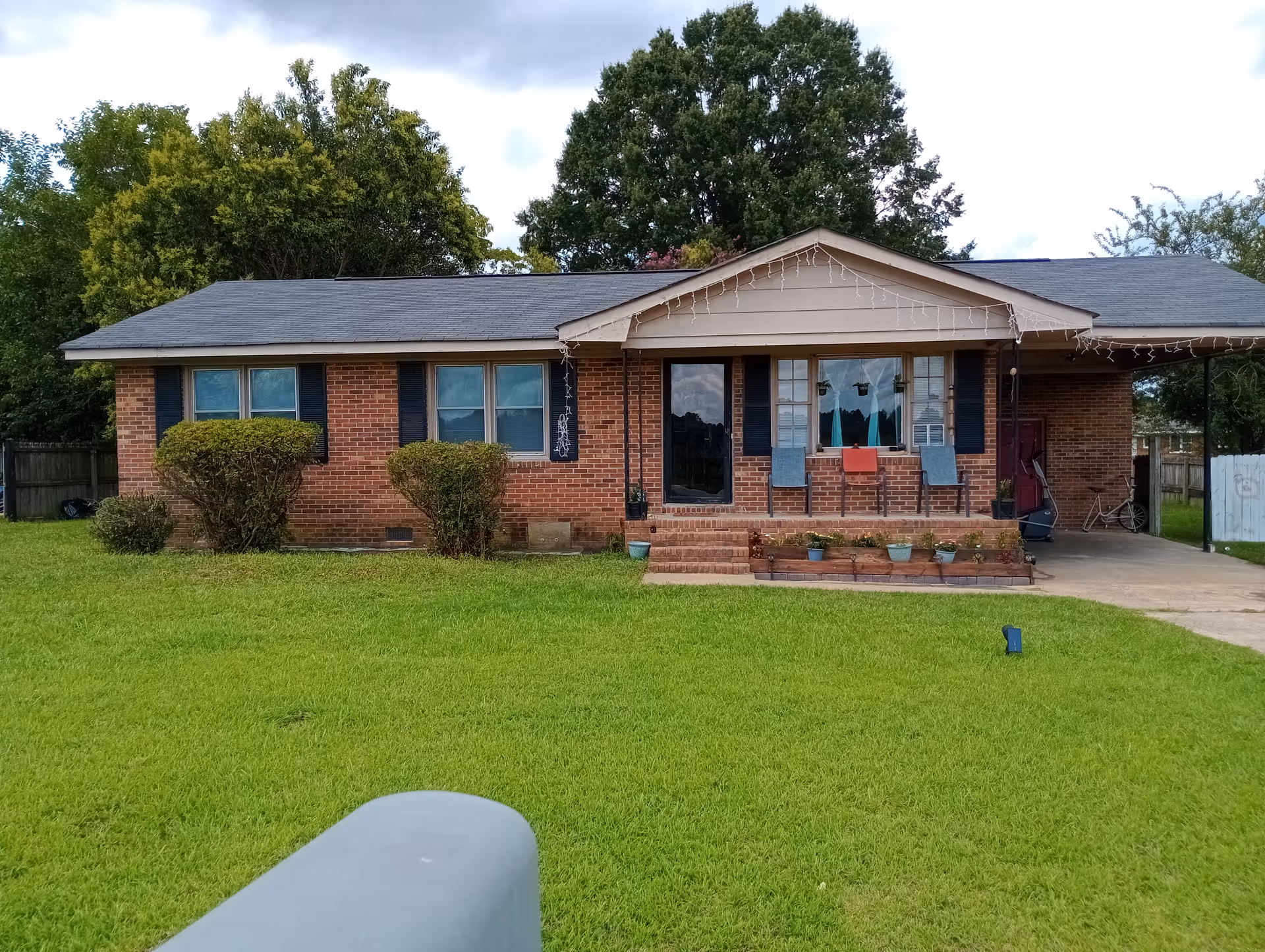Single-story brick house with front porch, string lights, and a green lawn