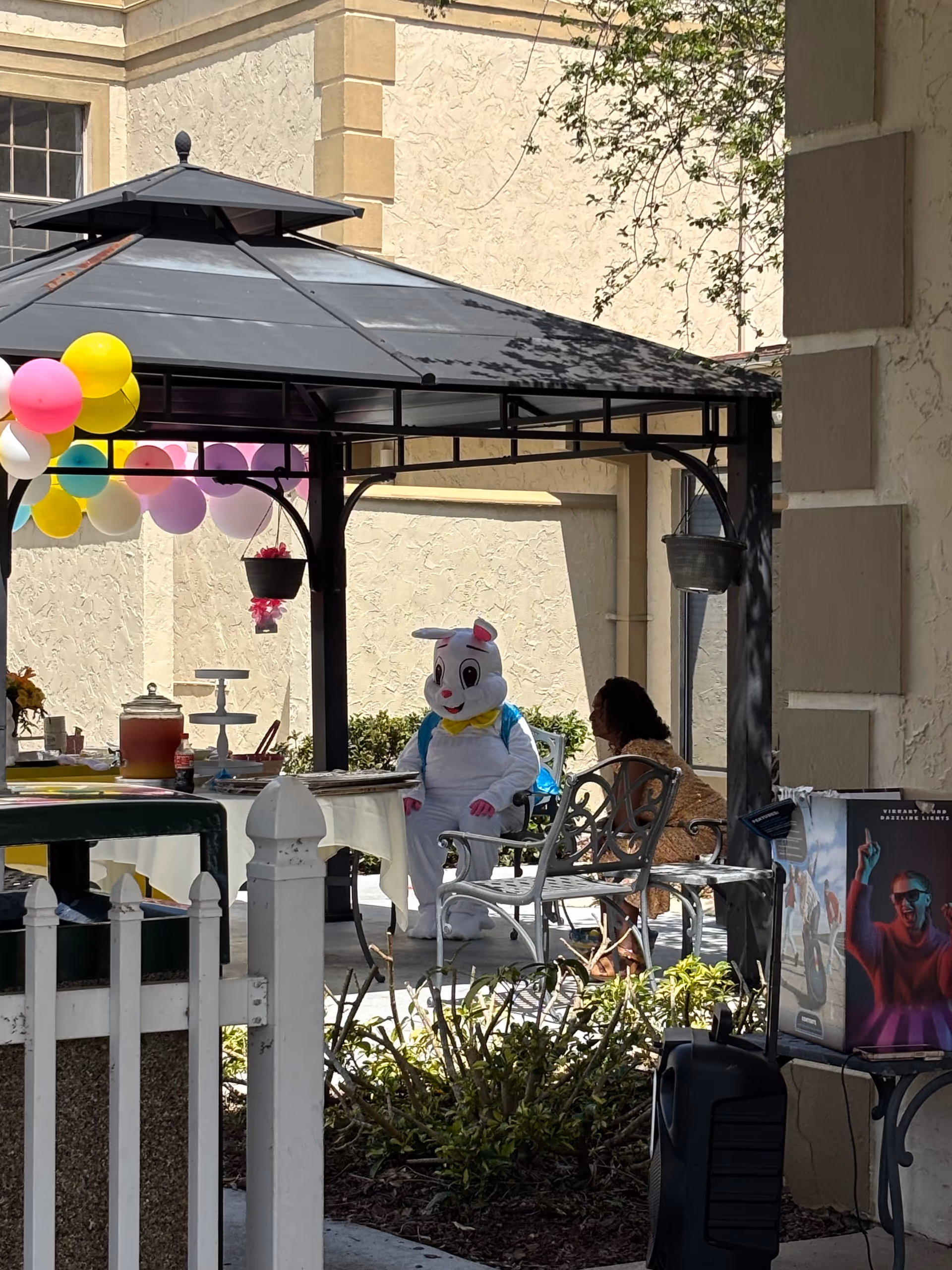 Outdoor patio at Bayview Center with balloons, costumed bunny, and residents seated.