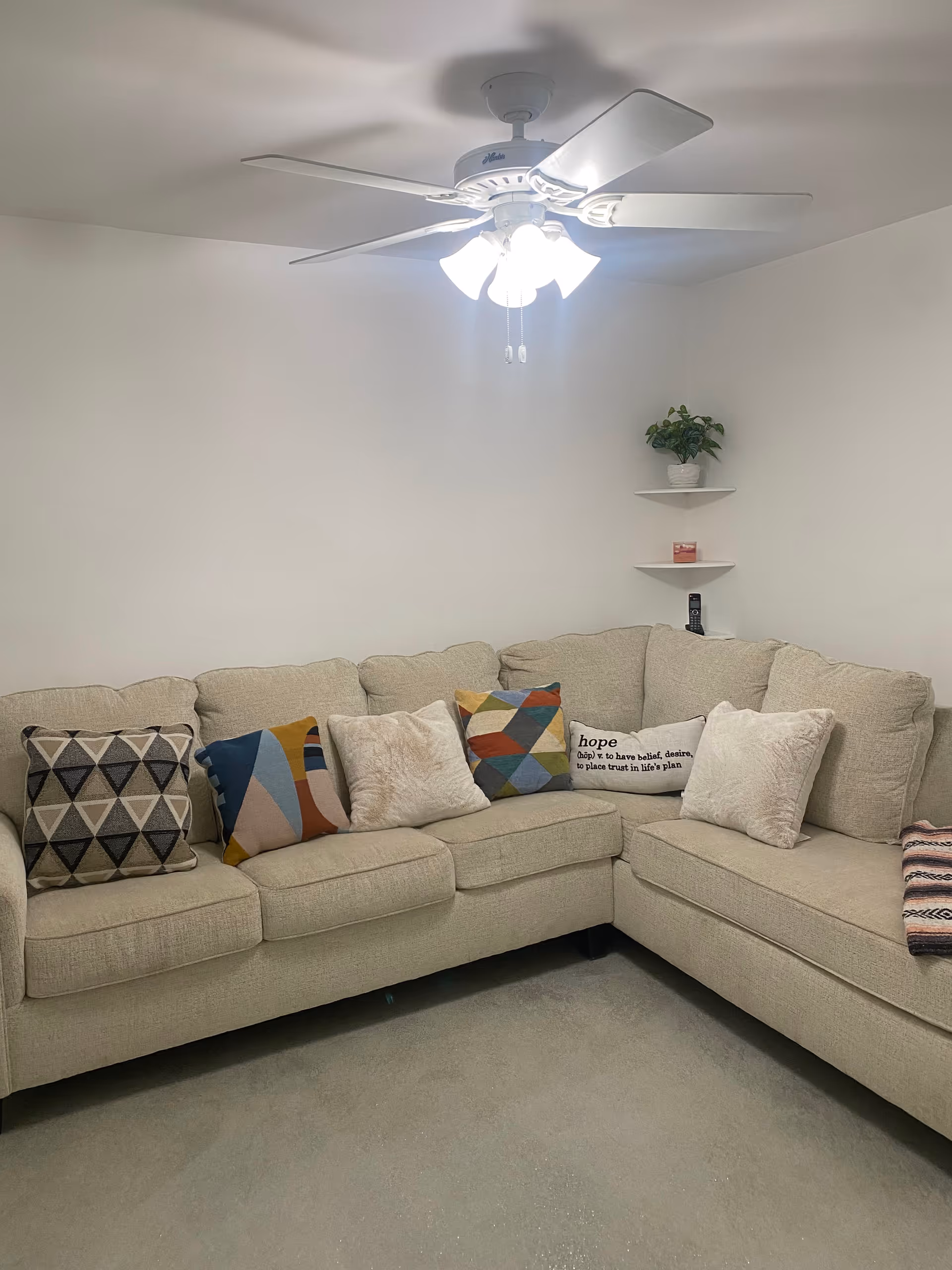Light-filled living room with beige sectional sofa, colorful cushions, and ceiling fan.