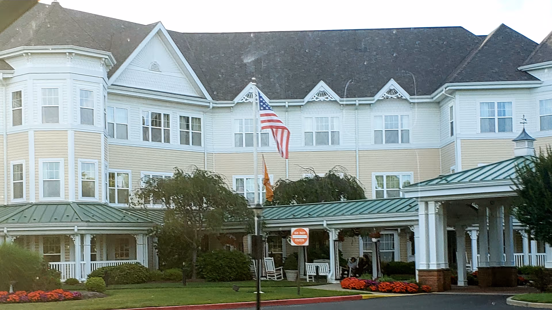 Sunrise of East Meadow exterior with porch, flags, and landscaping.