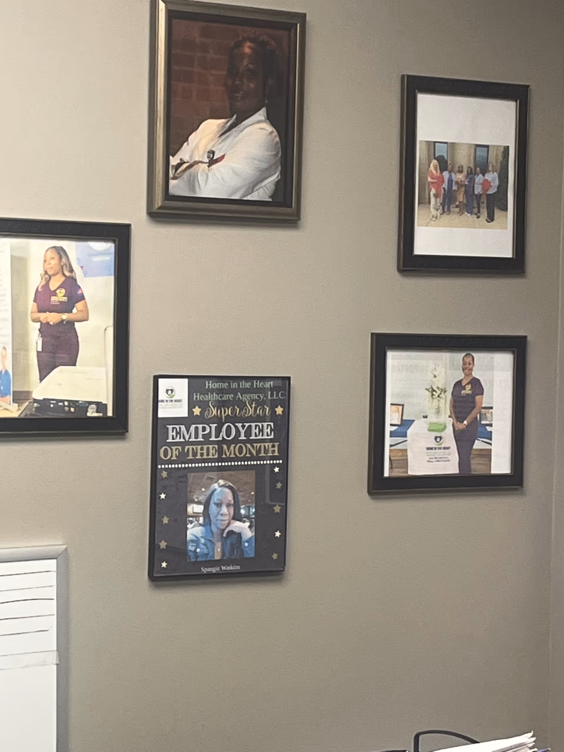 Interior hall wall with multiple framed photos and an Employee of the Month poster.