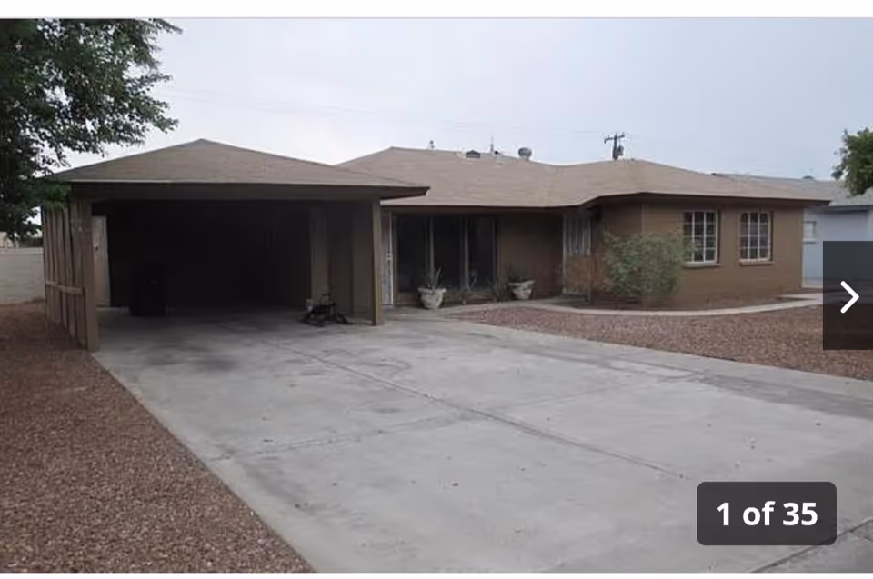 Single-story brown building with a carport, driveway, and desert landscaping.