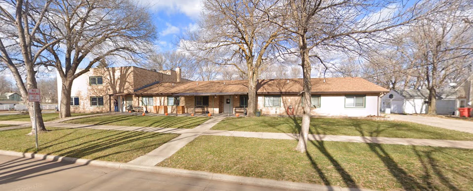 Single-story senior living building with a front lawn, trees, and a walkway.
